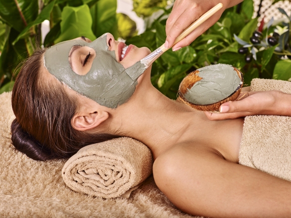 Woman with clay facial mask in beauty spa. In background tropica